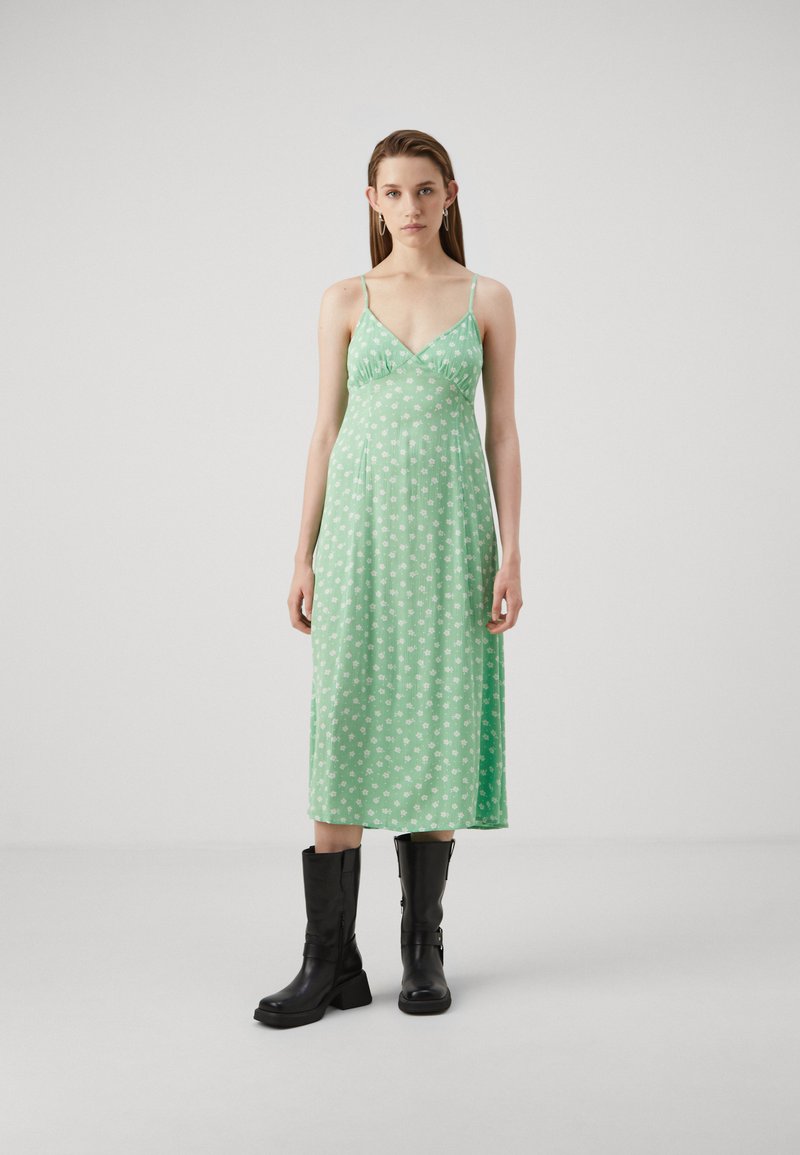 Vestido midi floral verde con tirantes finos y escote en V, combinado con botas negras hasta la rodilla. Tejido suave con una silueta fluida.