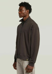 Donkerbruin half-zip sweatshirt met een relaxte pasvorm, ribbelmanchetten en een gestructureerd oppervlak. Bevat een klein logo op de zoom.