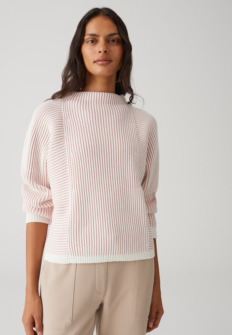 Maglione a coste con righe rosa e bianche, collo alto piegato e maniche morbide, abbinato a pantaloni beige.