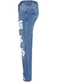 Jeans ajustados de color azul en tela de mezclilla, con parches desgastados en la pierna izquierda, bordes deshilachados y un diseño de cinturilla estándar.