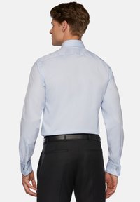 Camisa de vestir azul claro con mangas largas, puños abotonados y un cuello rígido. Presenta una textura suave y un diseño ajustado.