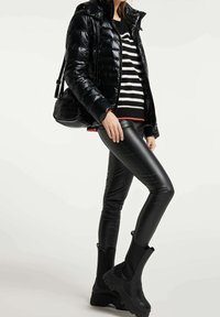 Sort pufferjakke, stribet sort og hvid sweater, sorte læderleggings og chunky sorte ankelstøvler. Tekstureret og tætsiddende design.