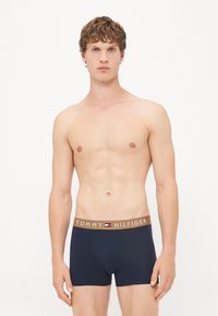 Navyblaue Baumwoll-Boxershorts mit einem braunen Gummibund, der das Logo "TOMMY HILFIGER" und ein kleines Flaggenemblem trägt.