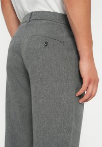 Graue, maßgeschneiderte Hosen aus strukturiertem Stoff, mit einer Gesäßtasche mit einem schwarzen Knopf und einem glatten Bund.