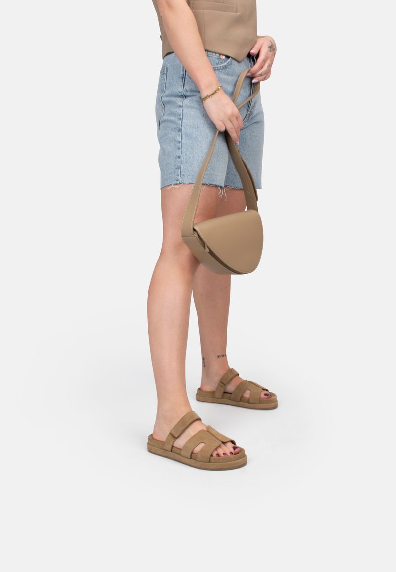 Tan schoudertas met een ronde vorm, een gladde leren textuur en een verstelbare schouderband. Gepaarde met denim shorts en bruine sandalen.