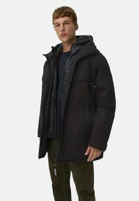 Sort isoleret jakke med lynlås foran, flere lommer og en aftagelig hætte. Lagdelt design med en blank inderside.