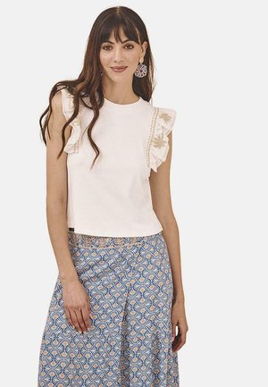 Top corto de algodón blanco con mangas con volantes, con costuras decorativas. Combinado con una falda azul estampada que muestra motivos en espiral.