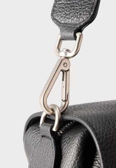 Ασημένιος γάντζος καραμπινέρ που συνδέει ένα ανάγλυφο μαύρο δερμάτινο λουράκι με μια μαύρη τσάντα από κόκκινο δέρμα με ορατό φερμουάρ.