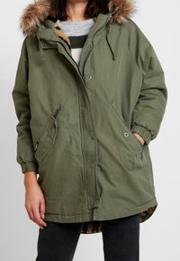 Olive green parka with a fur-lined hood, zip closure, and elastic cuffs. It features two side pockets and a patterned interior lining.