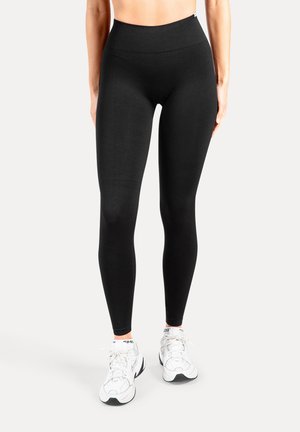Schwarze, hochtaillierte Leggings aus elastischem Stoff mit glatter Textur und enger Passform, kombiniert mit weißen Sportschuhen.
