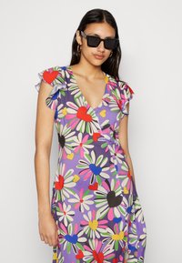 Vestido floral envolvente em roxo, com margaridas e corações coloridos, mangas com frufrus, decote em V e detalhes de botões na lateral.