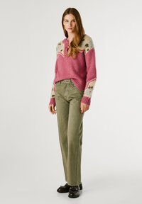 Suéter de mezcla de lana rosa con mangas estampadas, combinado con pantalones verdes oliva y zapatos negros con detalles metálicos. Pose de pie.