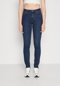 Jeans skinny azul escuro com alta cintura, feitos de denim. Inclui bolsos frontais e fecho de botão.