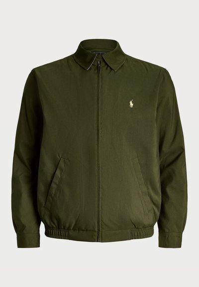 Veste zippée vert foncé avec un col pointu, des poches latérales, des poignets élastiqués et un petit logo brodé sur la poitrine. Texture de tissu lisse.