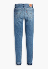 Jean en denim bleu clair vu de dos, avec deux poches arrière, des passants pour ceinture et un écusson de marque en cuir marron à la taille.