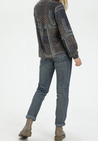 Blusa stampata con un motivo geometrico, tonalità blu e marrone, maniche lunghe, abbinata a jeans in denim scuro arrotolati e stivaletti alla caviglia marroni.