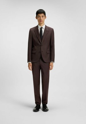 Brown tailored suit made of textured fabric, featuring two buttons, notched lapels, and matching trousers. Worn with a white shirt and black tie.