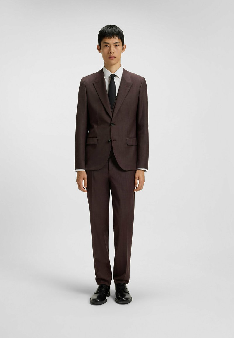 Brown tailored suit made of textured fabric, featuring two buttons, notched lapels, and matching trousers. Worn with a white shirt and black tie.