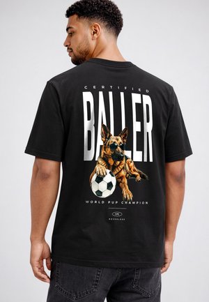 Young man wearing black T-shirt with a graphic of a German shepherd dog in sunglasses holding a soccer ball and text "Certified Baller."