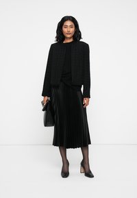 Crna teksturirana jakna, crni top, crna plisirana midi suknja, crne visoke potpetice i odgovarajuća torba. Jednostavna i elegantna monokromatska odjeća.