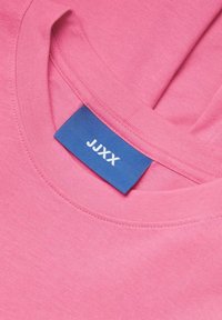 Rosa bomull T-skjorte med rund hals og korte ermer, med en blå etikett som viser "JJXX" sydd på siden.