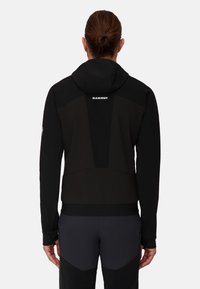 Black athletic jacket with a hood, featuring textured panels, a fitted design, and logo detailing at the back. Suitable for outdoor activities.