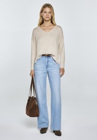 Beige V-nyakú pulóver, világoskék, bő szájú farmernadrág, barna velúr táska és hozzáillő bokacsizma. Puha anyag, laza fit és klasszikus dizájn.