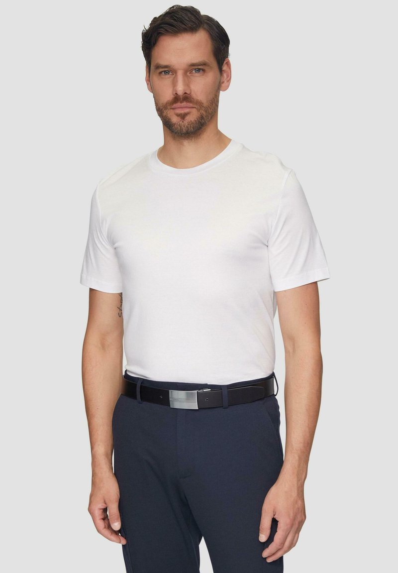 Weißes Kurzarm-T-Shirt, getragen mit marineblauen Hosen, ergänzt durch einen dunklen Gürtel mit einer silbernen Schnalle, der einen schlichten und klaren Look bietet.