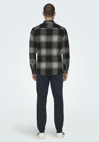 Zwart en grijs geruite flanellen shirt met lange mouwen, rechte zoom, knoopmanchetten en een klassieke kraag, gecombineerd met donkere broek.