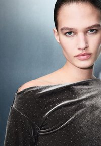 Tamnozeleni baršunasti gornji deo sa dizajnom bez naramenica, s suptilnim srebrnim akcentima i glatkom teksturom, na mekano osvetljenoj pozadini.