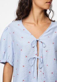 Blue and white striped blouse with short puff sleeves, v-neck, and front tie detail, adorned with small red cherry embroidery.