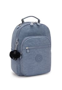 Zaino in tessuto grigio con forma arrotondata, tasca frontale con zip e un portachiavi a forma di scimmia nera pelosa. Presenta un logo circolare sul lato.