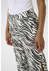 Pantaloni a gamba larga a strisce zebrate in bianco e nero con vita alta e spacchi laterali, realizzati in tessuto testurizzato, con una cintura liscia.