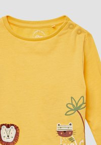 Gelbes Langarmshirt mit Illustrationen von Löwe und Tiger sowie zwei Druckknöpfen an der Schulter für einfaches An- und Ausziehen.