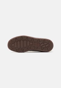 Brązowa podeszwa buta Puma z teksturowanym wzorem bieżnika i logo Puma na środku na białym tle.