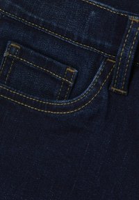 Denim azul oscuro con costuras visibles en amarillo, con un pequeño bolsillo para monedas en la parte delantera y una textura suave.