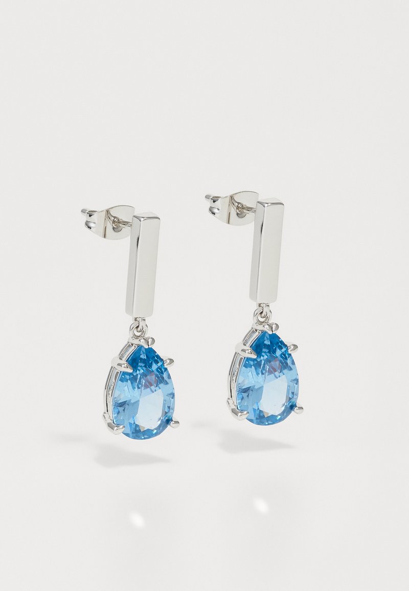 Sudraba pilienveida auskari ar caurspīdīgu, bumbierveida zilā dārgakmens elementu, kas karājas no taisnstūra formas pamatnes ar drošu aizdari.