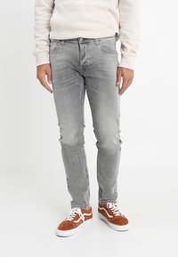 Grå denimjeans med slim fit, med en blekt tvätt, femficksdesign och kontrastsöm; bärs med bruna mockasneakers.