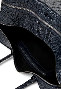 Bolso abierto de cuero negro con textura de cocodrilo que muestra un compartimento interior con cremallera y cierre de cremallera plateado.