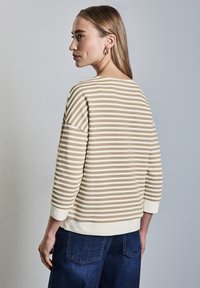 Gestreifter Pullover in Creme und Beige mit 3/4-Ärmeln, strukturiertem Stoff und rundem Ausschnitt, kombiniert mit dunkelblauen Jeans.