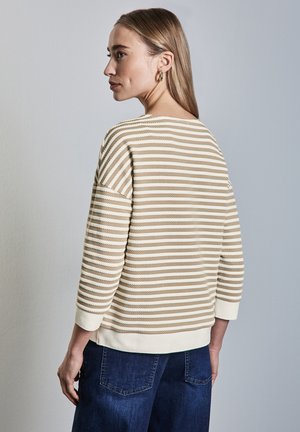 Sweter w paski w kolorze kremowym i beżowym z rękawami 3/4, teksturowany materiał oraz okrągły dekolt, zestawiony z ciemnoniebieskimi dżinsami.