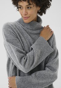 Grauer, gestrickter Pullover mit hohem, geripptem Kragen und weiten Ärmeln. Texturierter Stoff mit lässiger Passform und gerippten Bündchen, die das Design akzentuieren.