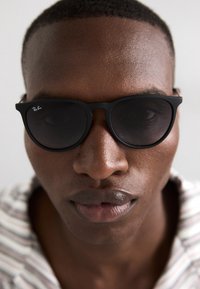 Ochelari de soare negri Ray-Ban cu ramă rotundă, lentile întunecate și finisaj mat, plasati pe un fundal neutru.