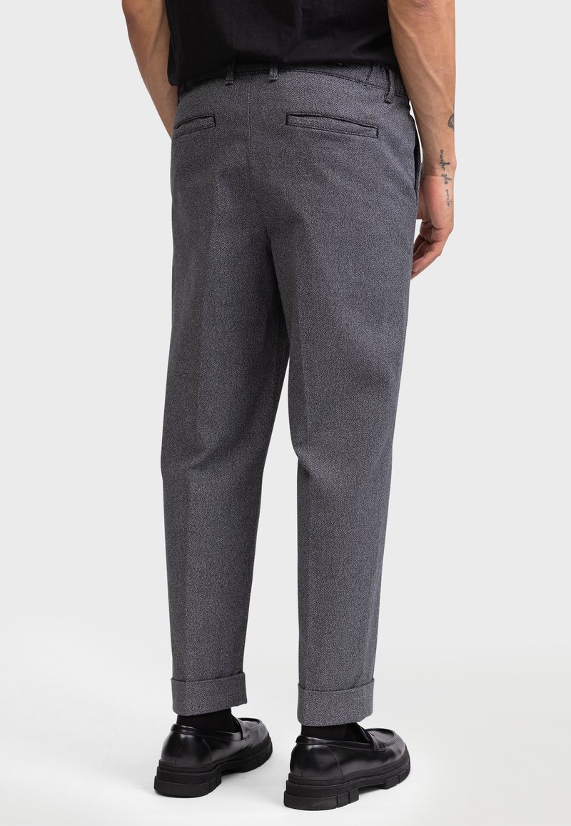 Pantalons gris texturés avec une coupe décontractée et des poignets repliés, dotés de poches arrière et associés à des chaussures noires.