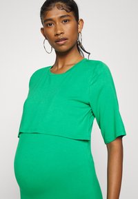 Top justo de mangas curtas, verde, com um design em camadas, feito de um tecido macio. Detalhes notáveis incluem um decote redondo e uma textura suave.