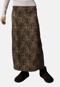 Jupe maxi imprimée léopard en beige avec des taches noires, faite de tissu doux. Elle présente une coupe droite et est assortie à des bottes marron foncé.