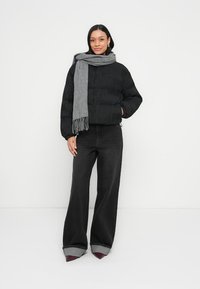 Μαύρο μπουφάν puffer με υφή, σε συνδυασμό με γκρι κασκόλ με κρόσσια. Σκούρο τζιν με φαρδιά παντελόνια και γυρισμένες άκρες, καθώς και παπούτσια με μυτερή μύτη.