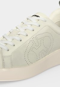 Λευκό sneaker χαμηλού προφίλ με λευκά κορδόνια, διάτρητο κυκλικό σχέδιο στο πλάι και παχιά υποσόλα σε εκρού απόχρωση.