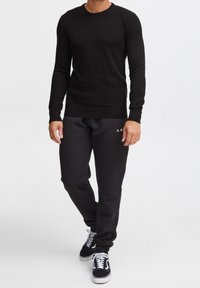 Czarny teksturowany sweter z dzianiny z długimi rękawami, zestawiony z czarnymi spodniami dresowymi z białym logo. Noszony z czarnymi tenisówkami.