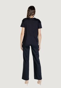 Camiseta de algodón negra de manga corta, ajuste relajado, combinada con pantalones anchos negros y tacones claros, vista desde la parte trasera.